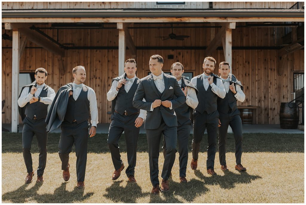 groom and groomsmen taking portraits in front of the barn at the bog