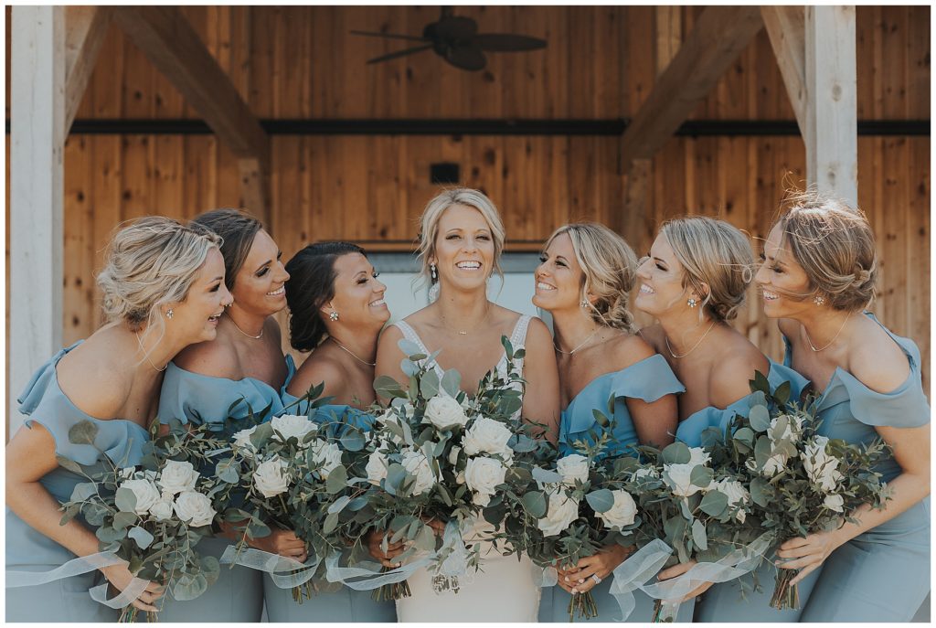 bride and bridesmaids wearing dusty blue dresses holding bouquets with white roses and eucalyptus