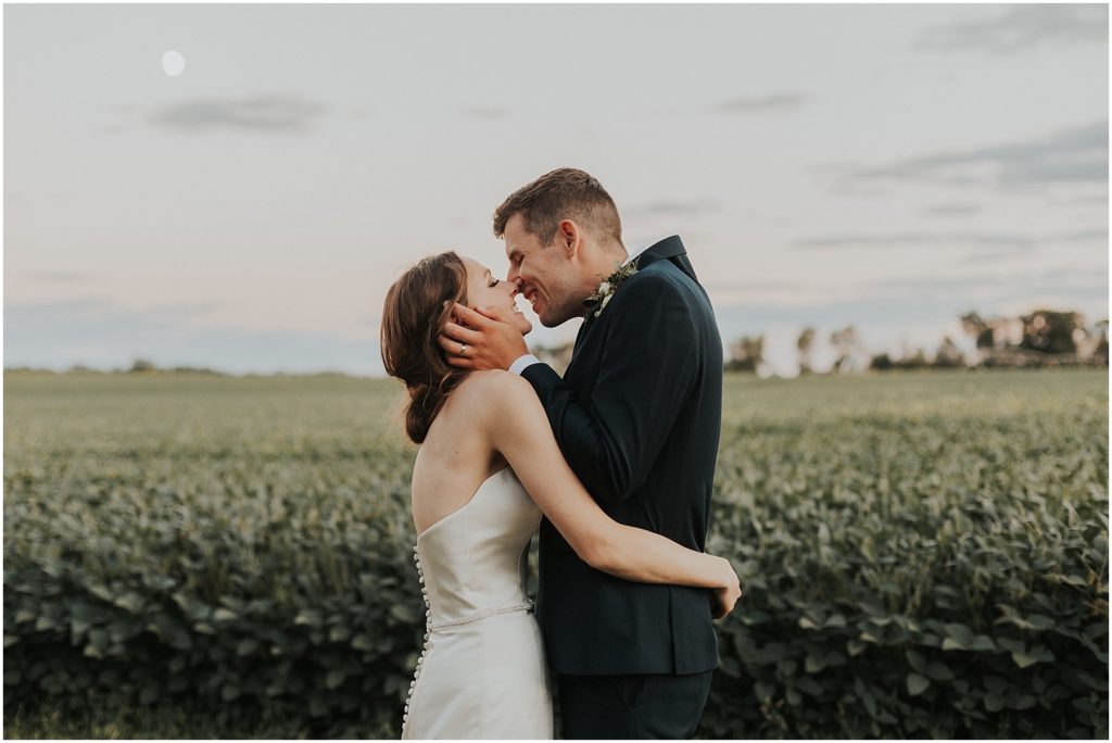 bride and groom holding each other in a field on their wedding day 