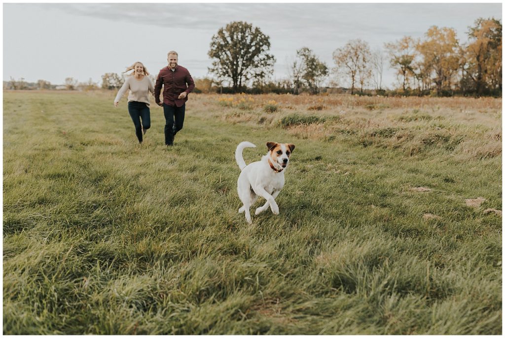 couple running through a field with their dog