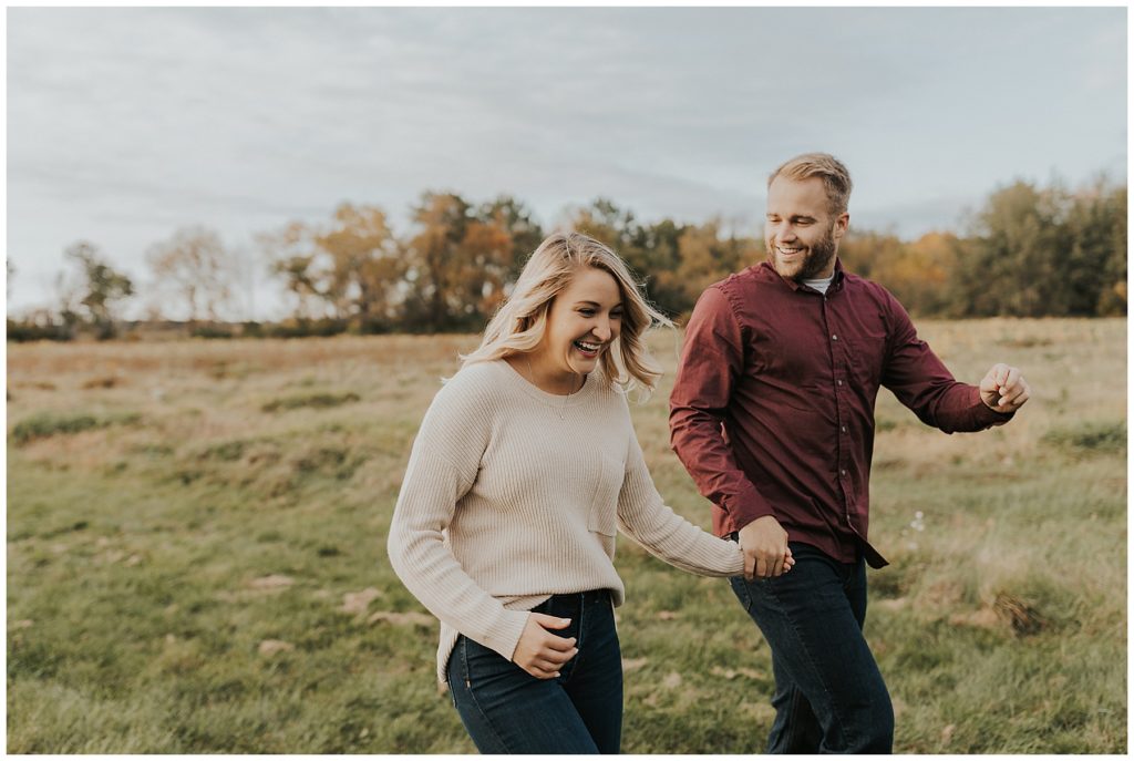 couple holding hands running through a field