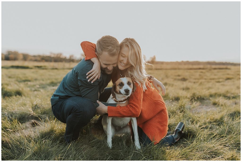 couple taking portraits and playing with their dog in a field during golden hour