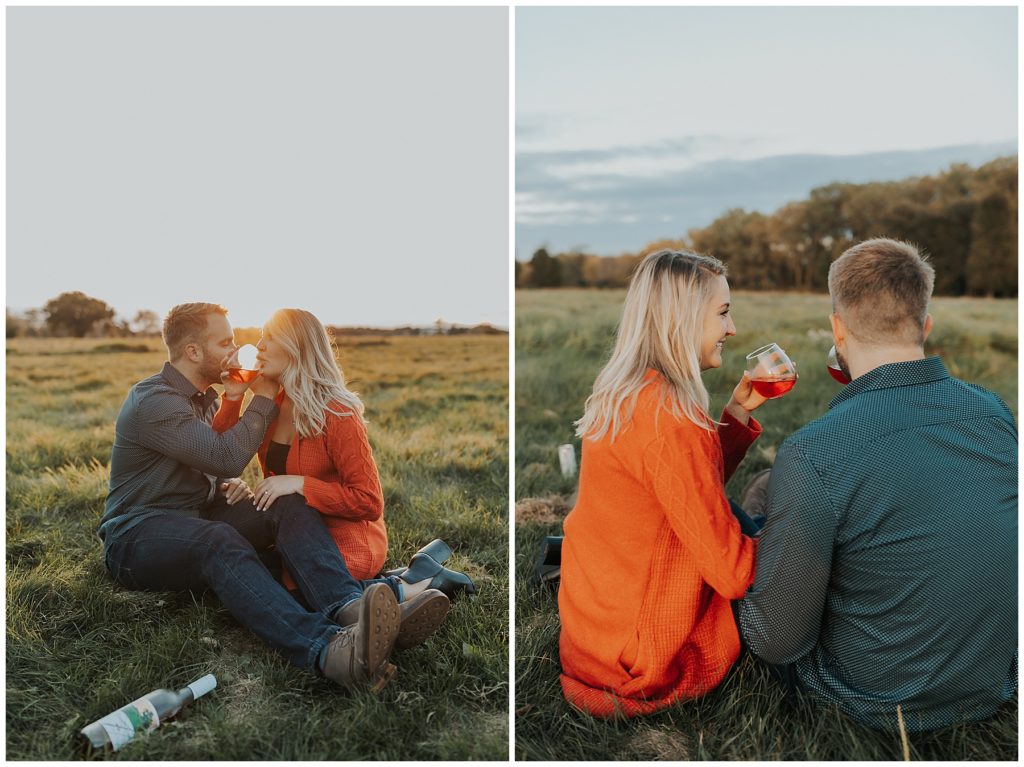 couple taking engagement photos and sipping wine in a field during golden hour