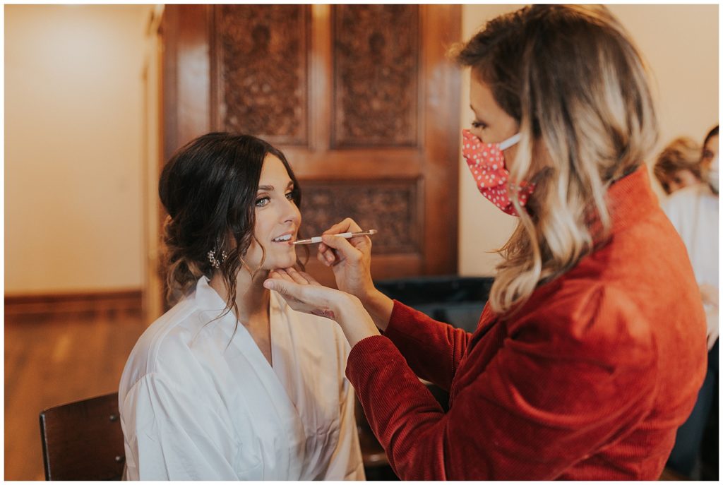 bride getting her makeup done while wearing a silk robe on her wedding day