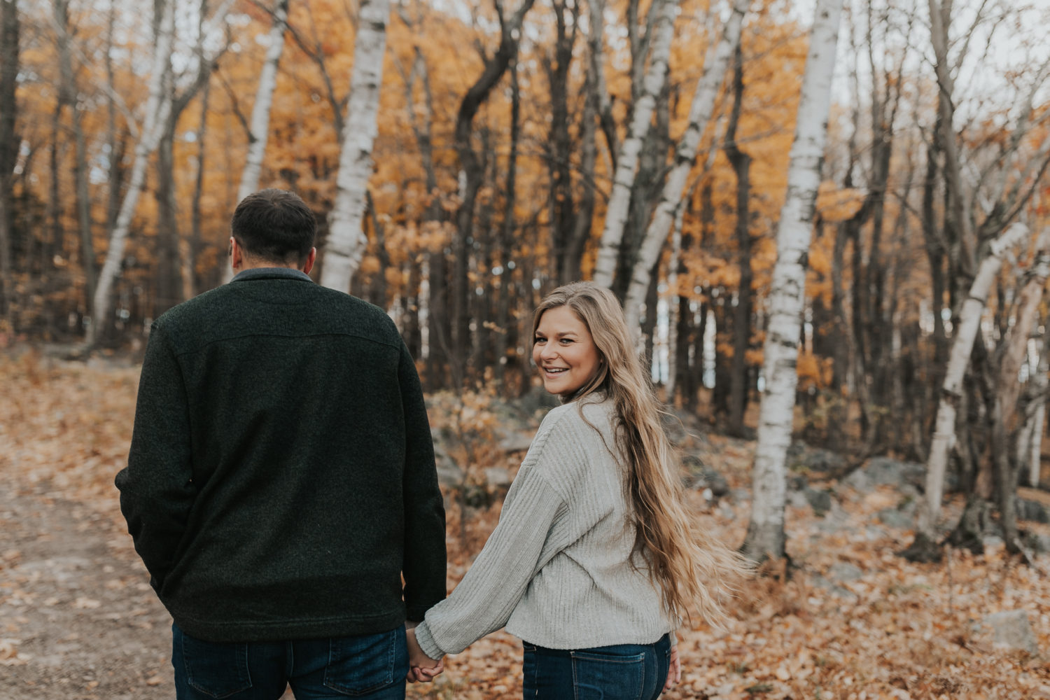 engaged couple holding hands and taking photos in the fall leaves in rib mountain state park